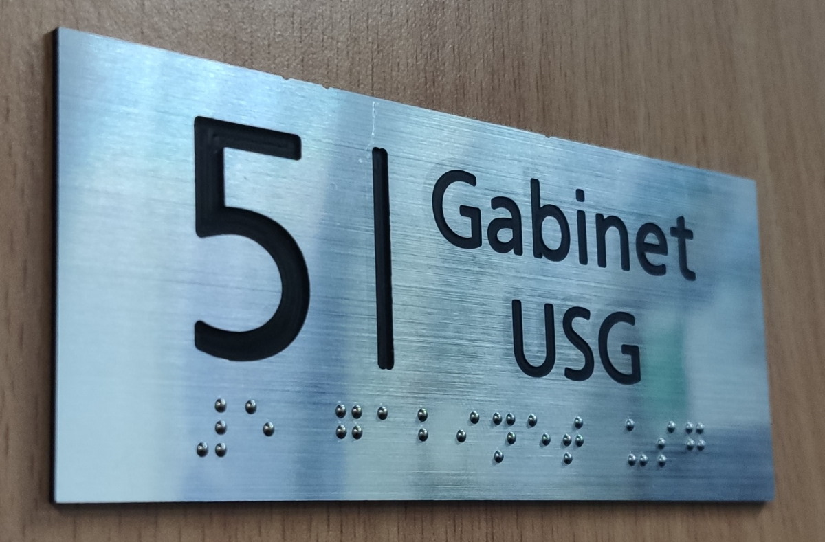 Zdjęcie przedstawia tabliczkę z grawerem i napisem w braju Gabinet USG